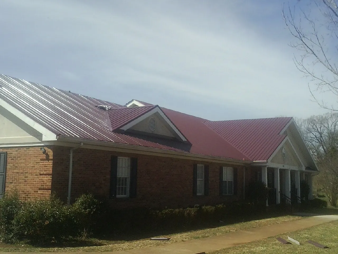 Red metal roof with gabled entries on a long brick building, from a Hail Damage Roof Repair job in Blackville