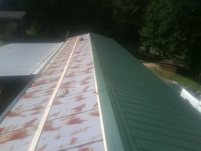Old rusted panels beside newly installed green metal roofing — Wind Damage Roof Repair by Roofing Brothers in Blackville