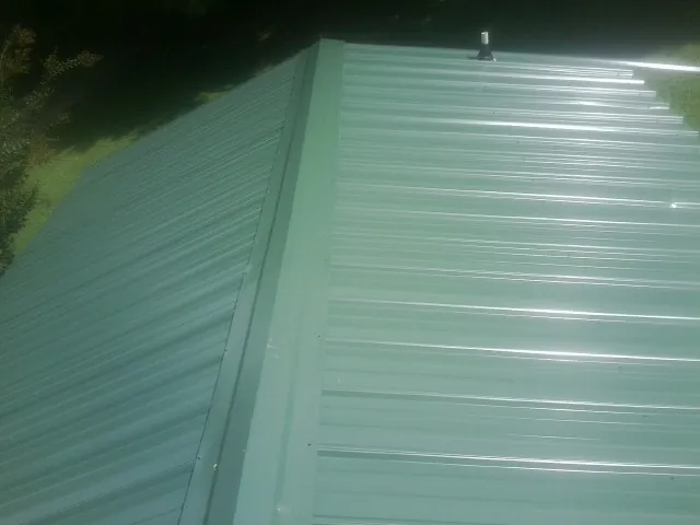 New green metal panels meeting at the ridge of a roof — Flat Roof Repair work by our crew in Blackville