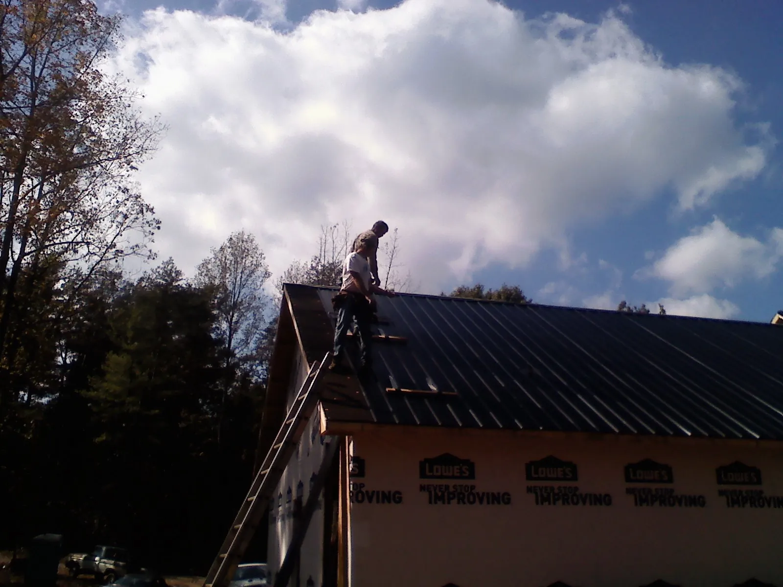 Roofer fastening dark metal panels high against a cloudy sky, from a Roof Inspection job in Blackville