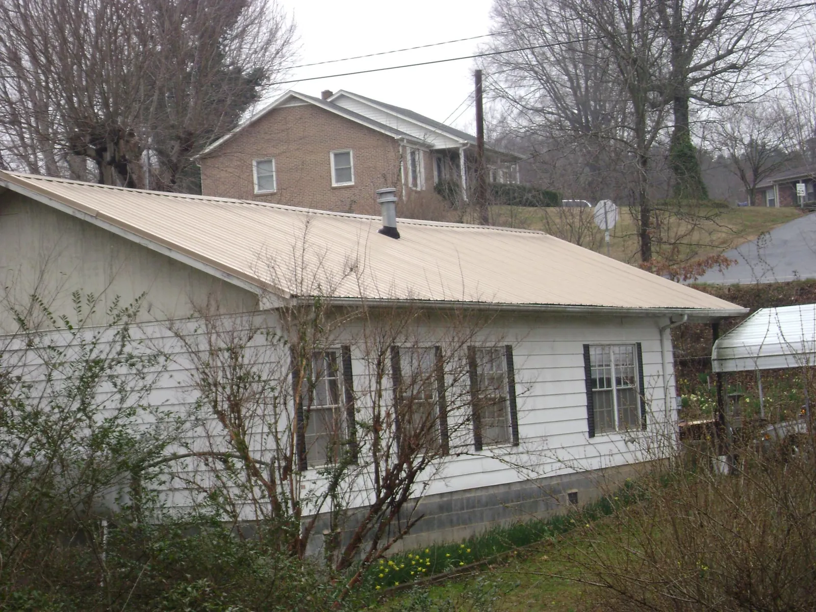 Tan metal roof on a white sided house set into a hillside — Commercial Roofing by Roofing Brothers in Blackville